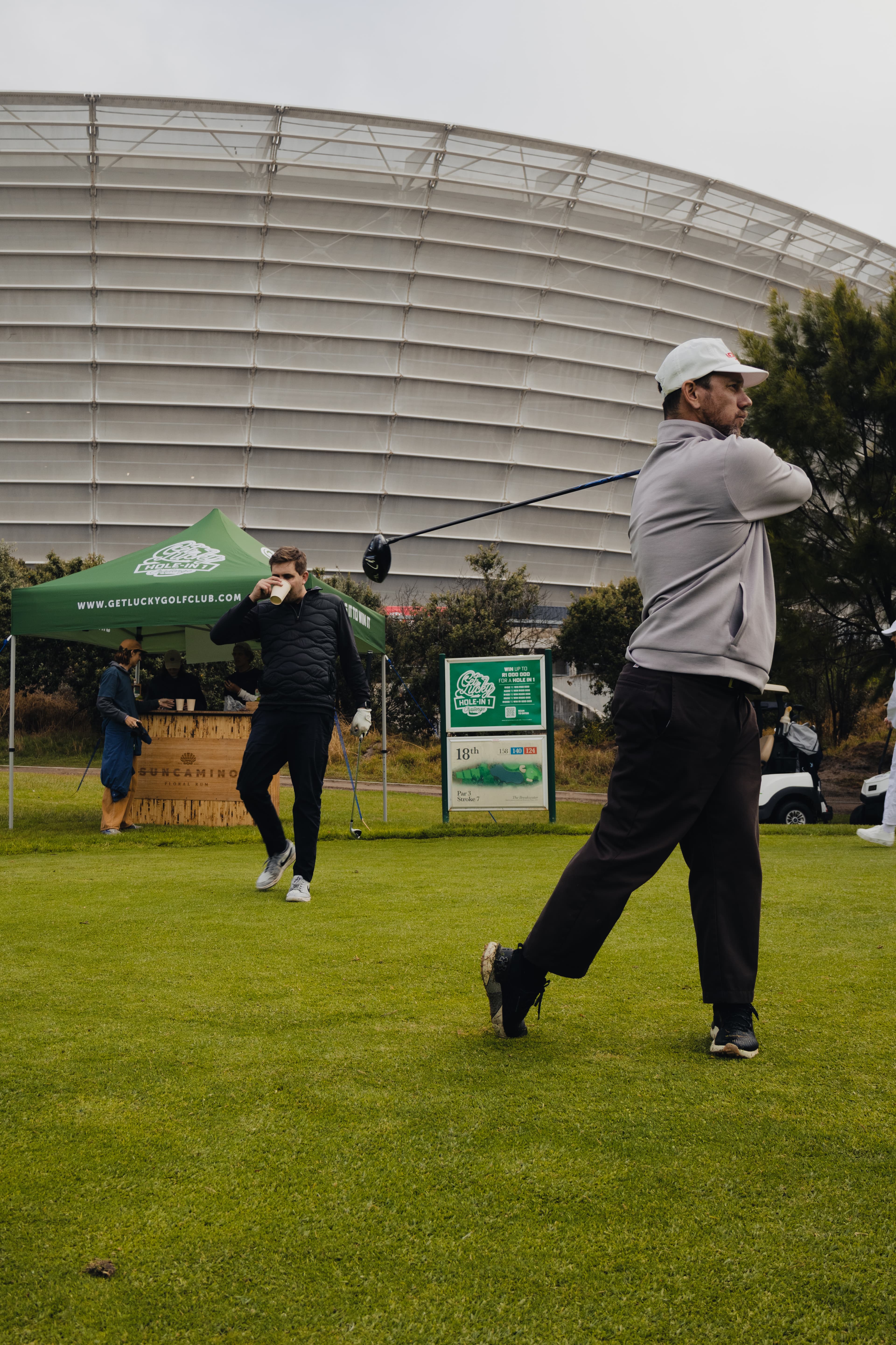 Golfer mid-swing with Cape Town Stadium and Get Lucky gazebo
